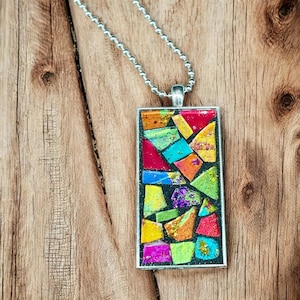 May include: A rectangular pendant necklace with a mosaic design. The pendant features a silver frame and a colorful mosaic of red, blue, green, yellow, and purple pieces. The necklace has a silver ball chain.