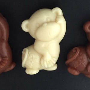 Puede incluir: Tres pequeñas figuritas de mono hechas de jabón. Una es blanca y las otras dos son marrones. Cada mono se tapa un ojo con la mano.