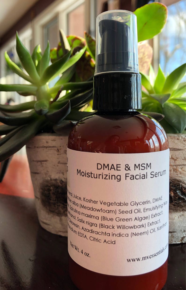 Puede incluir: Una botella de vidrio marr&oacute;n con una etiqueta blanca que dice "DMAE & MSM Suero Facial Hidratante". La botella tiene una tapa de bomba negra y contiene 118 ml de suero.