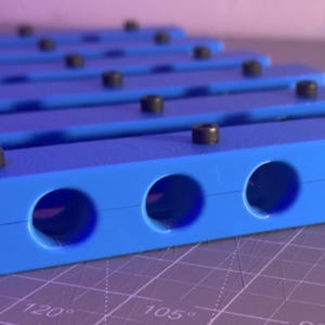 May include: A set of blue plastic pipe clamps with six holes each. The clamps are stacked on top of each other.