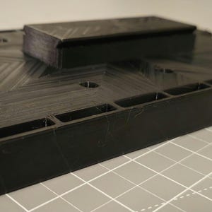 May include: A black plastic storage organizer with multiple compartments. The organizer has a textured surface and a raised section on top.