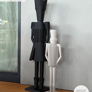 Könnte beinhalten: Zwei moderne, 3D-gedruckte Dekorfiguren. Eine ist schwarz mit einem kronenartigen Oberteil und einem plissierten Oberteil, die auf einem schwarzen Sockel steht. Die andere ist weiß mit vertikalen Streifen und steht auf einem weißen Sockel. Der Text "MODERN 3D PRINTED DECOR" ist sichtbar.