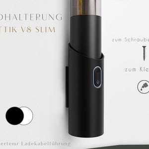 May include: A black wall-mounted device with a silver top and a curved holder. The device has a power button with a blue light. Text on the wall reads "WANDHALTERUNG FANTTIK V8 SLIM" and other German text.