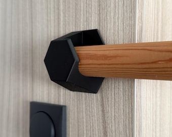 May include: A black, geometric door handle with a wooden dowel. The handle is mounted on a light wood-grain door. A matching black square plate with a circular inset is also visible.
