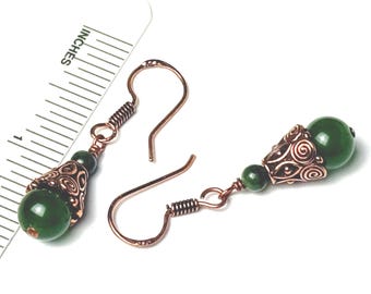 May include: A pair of copper-colored earrings with green beads. Each earring features a decorative, filigree-style cone and a large, round green bead. The earrings are shown with a ruler marked in inches.