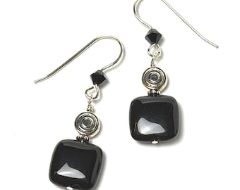 May include: A pair of dangle earrings featuring square, glossy black beads. Each earring has a silver-tone hook, a small black bead, and a silver-tone circular accent. The earrings are displayed against a white background.
