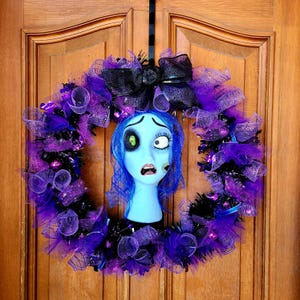 May include: A purple, black, and blue Halloween wreath with a blue and white Sally doll head from the Nightmare Before Christmas movie.