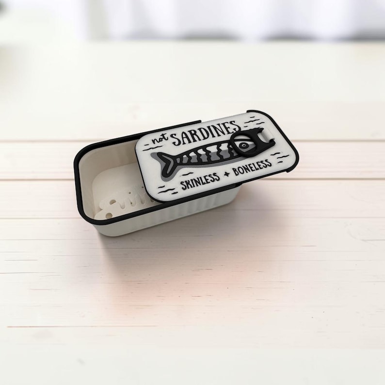May include: A rectangular off-white container with a black rim and a matching lid. The lid features a black graphic of a fish and the text "not SARDINES" and "SKINLESS + BONELESS" with a black pull-tab design printed on the top surface.