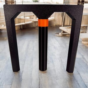 May include: A black metal stand with an orange band around the center post. The stand has two vertical bars that form a rectangular shape.
