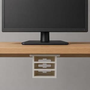 May include: A white under-desk storage organizer with three compartments is mounted under a wooden desk. A black computer monitor sits on the desk. The organizer is designed to hold small office supplies.