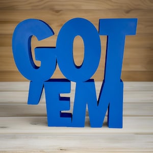 May include: Blue wooden letters spelling out "GOT 'EM" on a light wood background.