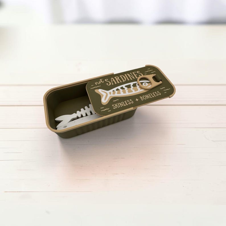 May include: An olive green rectangular container with a sliding lid featuring a white fish skeleton graphic and the text "not SARDINES" and "SKINLESS + BONELESS". A white fish skeleton utensil is visible inside the open container.