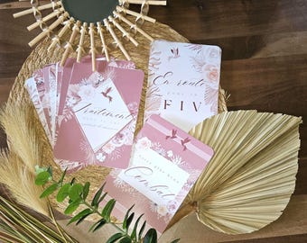 May include: Pink and white floral cards with the text "En route pour la FIV" and "Traitement" on them. The cards are on a woven mat with a fan made of dried palm leaves.