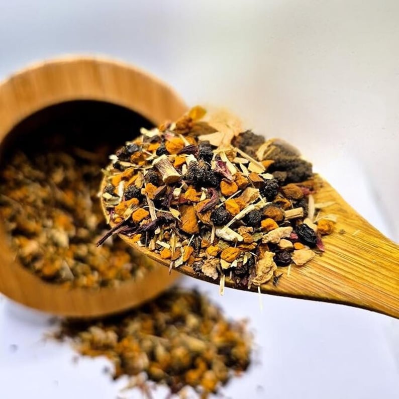 May include: A wooden spoon filled with a colorful blend of dried herbs and spices, including orange, brown, and purple elements. The spoon is held over a wooden bowl, with some of the mixture spilling out. The image is set against a white background.
