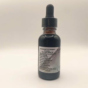 May include: A dark glass bottle with a black dropper top, filled with a dark liquid. A label on the bottle lists ingredients and usage instructions. The bottle is likely a herbal supplement or tincture.