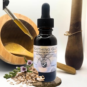 Puede incluir: Una botella de vidrio oscuro de gotas herbales "Soothing Gut" con un cuentagotas negro. La etiqueta dice "Gotas herbales concentradas y extraídas por: Old Revolution Herbals". La botella se encuentra sobre una pequeña plataforma de madera oscura, con un mortero y una maja de madera en el fondo.
