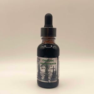 May include: A small, dark glass bottle with a black dropper top. The bottle contains a dark liquid and has a label with the words "ORGANIC INGREDIENTS" and other text. The bottle is on a white background.