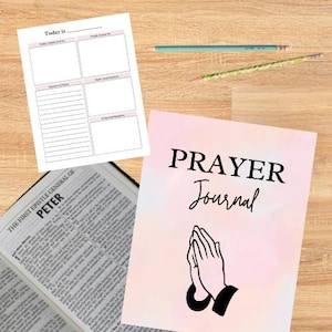 May include: A pink and white prayer journal with the words "PRAYER JOURNAL" in black text. The cover features a black illustration of two hands clasped in prayer.