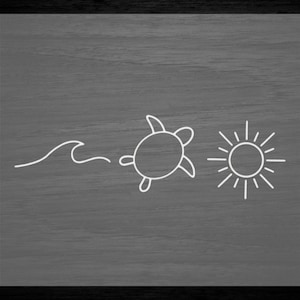 May include: A white line drawing of a wave, a turtle, and a sun on a gray wood background.