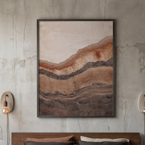 May include: A framed rectangular wall art piece featuring abstract layered earth tones in shades of rust, brown, and cream, displayed above a wooden bed frame with sage green, charcoal, and terracotta bedding and a round brown leather pillow.