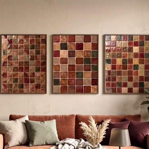 May include: Three rectangular wall art pieces featuring a grid of square tiles in shades of red, brown, green, and cream. Each piece is framed in a thin, dark border, displaying a glossy, textured finish across the individual tile surfaces.