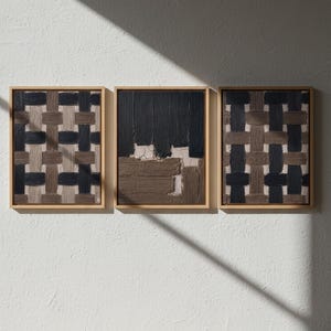 以下が含まれることがあります： 3つの額装された抽象芸術作品。アートワークは、茶色、黒、ベージュの色合いの織り模様を特徴としています。フレームは明るい木の色で、作品は白い壁に展示されています。太陽光の影が壁に落ちています。