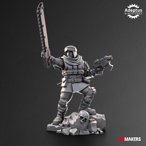 May include: A gray miniature soldier figure standing on a rocky base with a skull. The figure wears a helmet, scarf, and tactical gear, holding a long chainsword raised in one hand and a pistol in the other. Text reads Adeptus Miniatures and RED MAKERS.