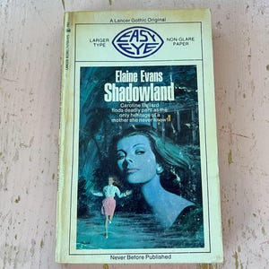 May include: Vintage paperback book titled "Shadowland" by Elaine Evans. The cover features a woman's portrait in blue tones, a running figure, and the text "Caroline Ballard finds deadly peril as the only heritage of a mother she never knew!"
