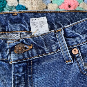 May include: Close-up of the waistband of a pair of blue denim jeans with a care label attached. The label reads "Machine wash warm normal cycle only non-chlorine bleach, tumble dry hot, hot iron if needed, wash and dry with like colors, WPL 423, 852 13, 581 0698 58189-5, 552".