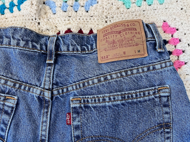 May include: Blue denim jeans with a Levi's label on the back pocket. The label reads "Levi Strauss & Co. Original Riveted Quality Clothing" and "512" Slim Fit Straight Leg.