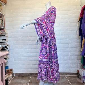 May include: A floor-length maxi dress featuring a vibrant geometric and mandala-inspired pattern in shades of bright pink, purple, blue, and white. The garment has wide, flowing kimono-style sleeves and a tiered skirt design with a relaxed silhouette.