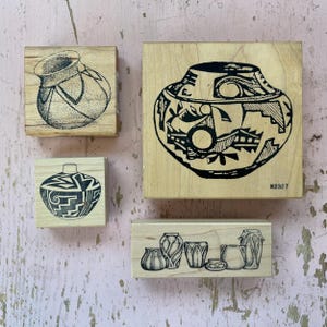 May include: Four wooden stamps with black ink designs of pottery. The stamps are various sizes and shapes, including a large square stamp with a detailed pot design and the number 2327. The other stamps feature different pottery styles.
