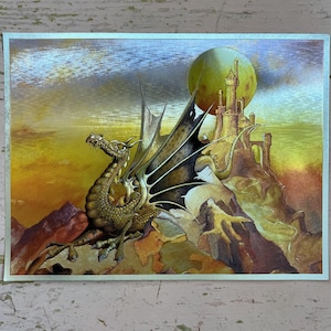 May include: A rectangular print featuring a golden dragon with large, dark, spiky wings perched on a rocky cliff. In the background, a tall stone castle stands against a large, glowing yellow moon, set against a gradient sky of orange and blue.
