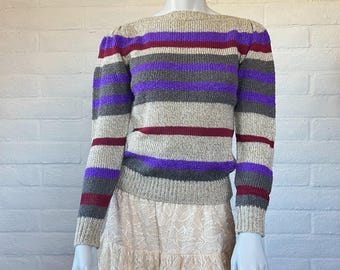 May include: A beige, long-sleeved sweater with horizontal stripes in shades of purple, gray, and burgundy. The sweater has a round neckline and is displayed on a mannequin. The bottom half of the mannequin is wearing a cream-colored lace skirt.