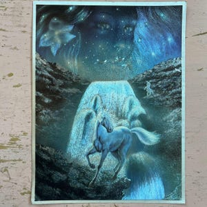 May include: A fantasy art print featuring a blue unicorn standing before a waterfall. The artwork has a celestial theme with a starry night sky, a large face, and a flower-like shape. The color palette is primarily blue and black.