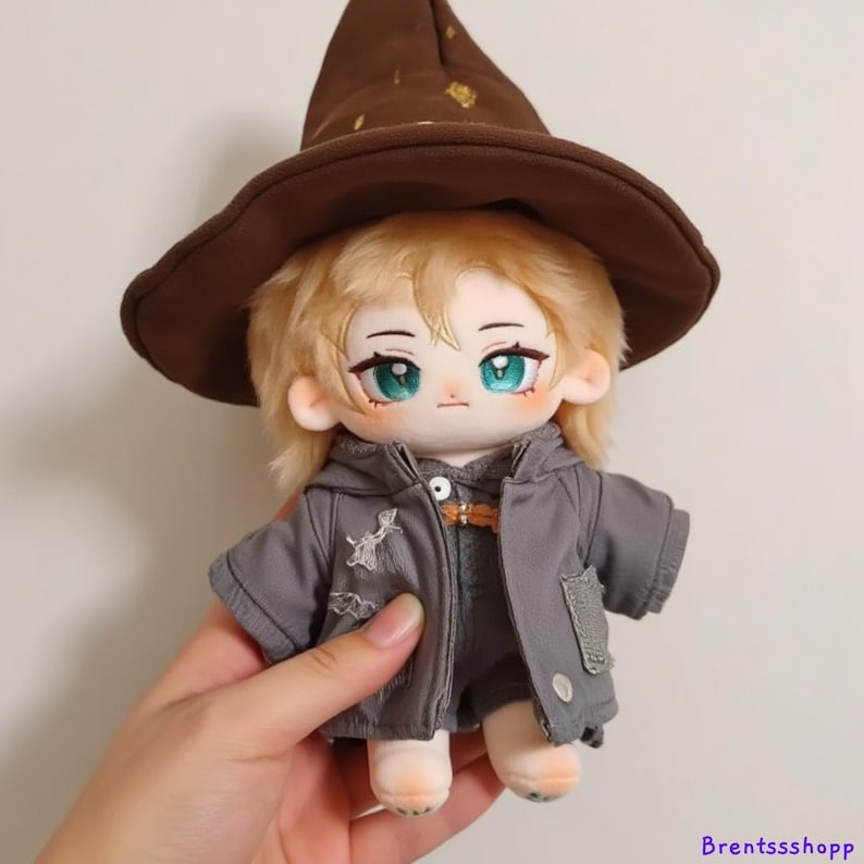 May include: A plush doll wearing a brown pointed hat with gold stars, a gray hooded jacket, and light brown pants. The doll has blonde hair and blue eyes.