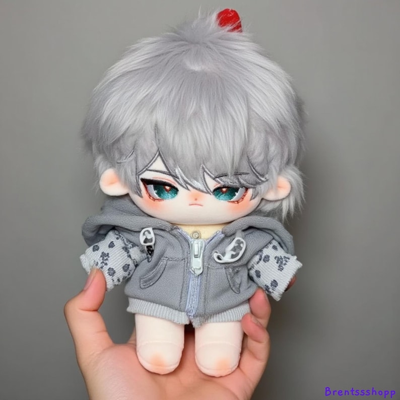 May include: A gray plush doll with silver hair, wearing a gray hooded sweatshirt with a white and gray pattern. The doll has blue eyes and a red detail on its head.