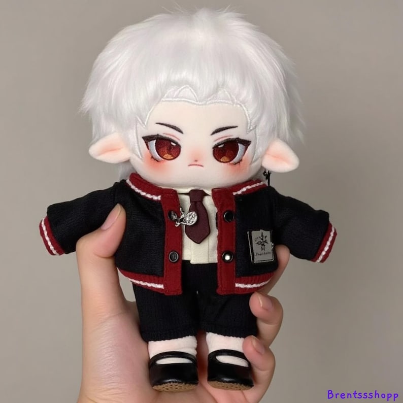 May include: A plush toy with white hair, red eyes, and a black and red outfit. The toy is wearing a black jacket with red trim, a white shirt, a red tie, and black pants. The toy is holding a silver charm necklace.