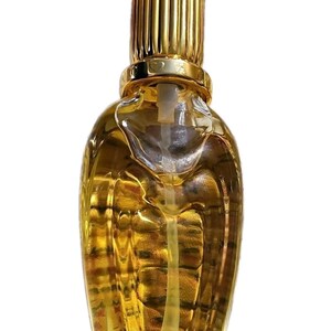 May include: A clear glass perfume bottle filled with amber-colored liquid, featuring a textured, wing-like design on the body. The bottle is topped with a cylindrical, vertically ribbed gold-toned cap and a smooth gold-toned collar.