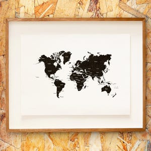 May include: A framed world map print. The map is black and white, with continents filled in black and country names labeled in black. The print is set against a white background and framed in a light brown wooden frame. The background is a textured wood.