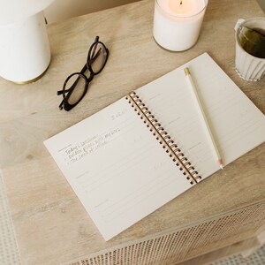 May include: A white spiral bound notebook with a pencil on top of it. The notebook has the date 5/12/20 written on the top page. The text "Today's sunshine - Outdoor picnic with my boys - The smell of coffee" is written on the page.