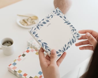 May include: A white notepad with a blue floral border. The notepad has the word "notes" written on it.