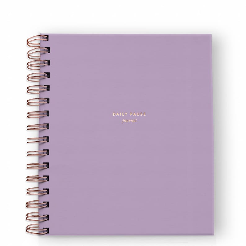 May include: A square, lavender-colored journal with a copper spiral binding. The words "DAILY PAUSE journal" are printed in gold on the front cover. The journal is new and unused.