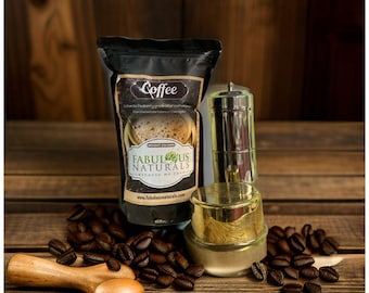 Puede incluir: Una bolsa de café negra con el texto "Coffee" y "Fabulous Naturals" en ella. La bolsa está sobre una superficie de madera con un filtro de café plateado y dorado a su lado. Hay granos de café esparcidos alrededor de la bolsa y el filtro.