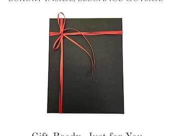 May include: A black square gift box tied with a red ribbon. The box has the text "LUXURY INSIDE, ELEGANCE OUTSIDE" and "Gift-Ready, Just for You". The ribbon is tied in a bow on top of the box.