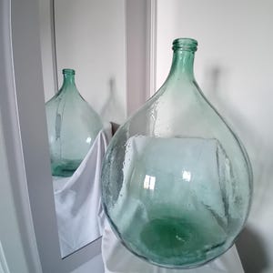 A select rustic Italian demijohn, transparent with green hues and microbubbles, holds 54 liters. A vintage furnishing accessory.
