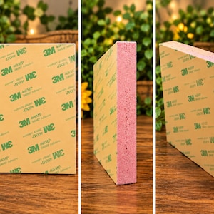 Può includere: Un blocco rettangolare di schiuma rosa con un supporto adesivo color marrone chiaro su un lato. La superficie adesiva è coperta da una carta protettiva stampata con il logo adesivo 3M 468MP verde in un motivo ripetuto su tutta la superficie.