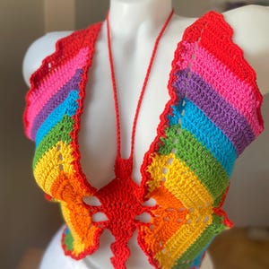 Könnte beinhalten: Ein Regenbogen-Crochet-Top mit einem Schmetterlingsdesign in der Mitte. Das Top ist aus verschiedenen Farben gefertigt, darunter Rot, Orange, Gelb, Grün, Blau, Lila und Pink.