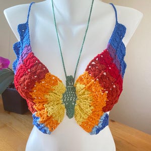 May include: A rainbow crochet top shaped like a butterfly. The top is made with a variety of colours, including red, orange, yellow, green, blue, and purple.