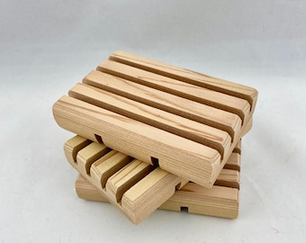 May include: Three natural wood soap dishes stacked on top of each other. The dishes have a slatted design to allow soap to drain.
